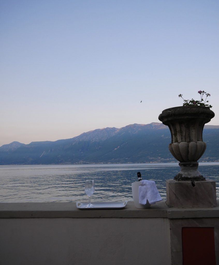 L'aperitivo è servito, il cestello con il vino fresco, il bicchiere sul vassoio sono pronti su una terrazza quasi a sfioro sul Lago di Garda Bresciano